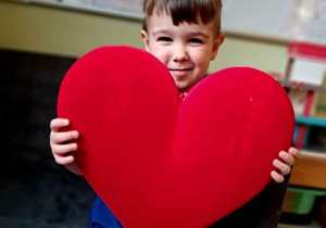 Chłopiec pozuje do zdjęcia trzymając w dłoniach duże czerwone serce