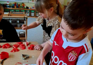 Chłopiec posypuje swoje serce solą morską w kolorze czerwonym, w tle widać dziewczynkę malująca farbami serce uformowane z masy solnej