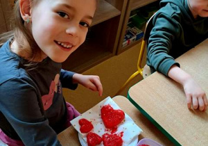 Dziewczynka posypuje serca uformowane z masy solnej solą morską w kolorze czerwonym