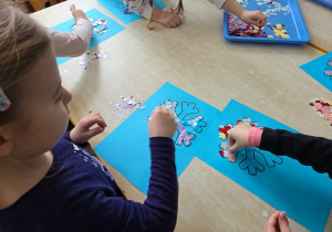 Dzieci wyklejają śnieżynkę kolorowymi cekinami