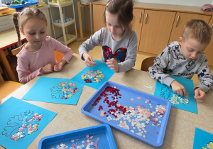 Dzieci wyklejają śnieżynkę kolorowymi cekinami