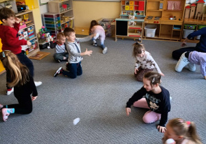 Dzieci na dywanie rzucają się papierowymi śnieżkami w rytm muzyki