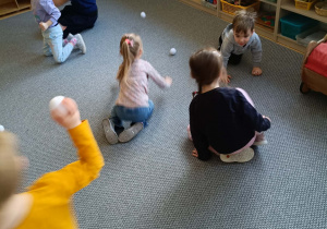 Dzieci na dywanie rzucają się papierowymi śnieżkami w rytm muzyki