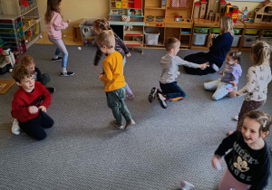 Dzieci na dywanie rzucają się papierowymi śnieżkami w rytm muzyki