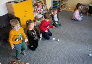 Dzieci na dywanie rzucają się papierowymi śnieżkami w rytm muzyki