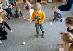 Dzieci na dywanie rzucają się papierowymi śnieżkami w rytm muzyki