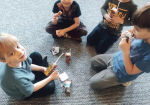 Chłopcy siedzą w kręgu, jedzą ciasteczka i piją sok.