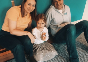 Rodzice siedzą na dywanie z córką.