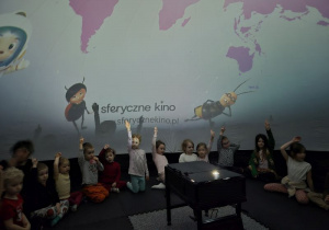 Dzieci siedzą w namiocie i czekają na rozpoczęcie seansu