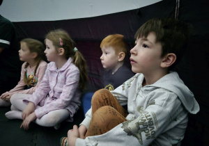 Dzieci siedzą w namiocie i czekają na rozpoczęcie seansu