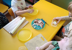 Dzieci siedzą przy stoliku, obierają jajka i robią z nich myszkę