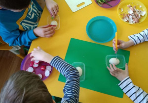 Dzieci siedzą przy stoliku, obierają jajka i robią z nich myszkę