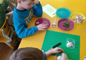 Dzieci siedzą przy stoliku i robią myszkę z jajka