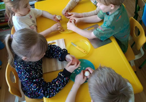 Dzieci siedzą przy stoliku i obierają jajka