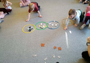 Dzieci sortują śmieci do odpowiednich pojemników.