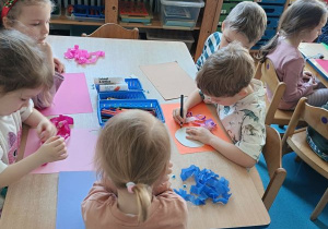 Dzieci wykonują pracę plastyczną przy stolikach