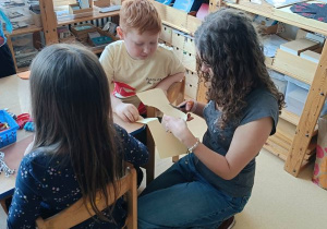 Dzieci wykonują pracę plastyczną przy stolikach