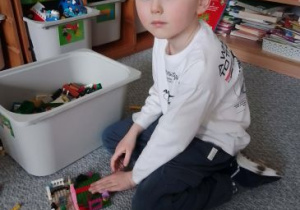 Chłopiec na dywanie buduje z klocków Lego