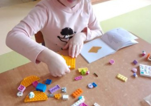 Dziewczynka przy stoliku buduje ze swoich klocków Lego
