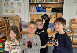Dzieci stoją obok siebie trzymając w rękach samochody zbudowane z klocków Lego