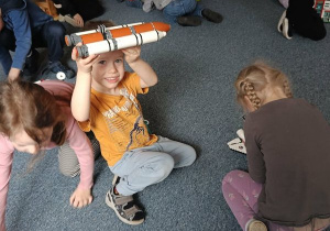 Chłopiec unosi do góry w dłoniach rakietę kosmiczną z klocków Lego