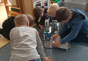 Dzieci siedzą na dywanie i układają komisariat policji z klocków Lego