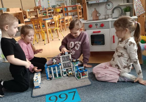 Dzieci siedzą na dywanie i układają komisariat policji z klocków Lego