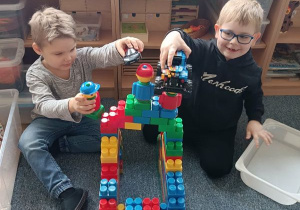 Chłopcy budują na dywanie budowlę z klocków