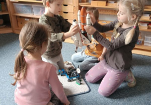Dzieci siedzą na dywanie i układają kosmos z klocków Lego