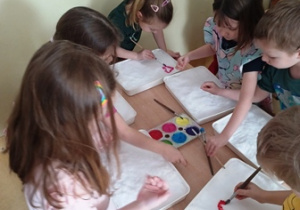 Dzieci stoją nad tacami wypełnionymi śniegiem i rozpoczynają malowanie farbami