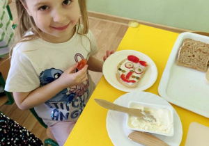 Dziewczynka siedzi przy stoliku i przygotowuje kanapkę