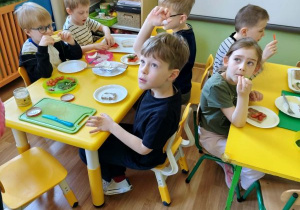 Dzieci siedzą przy stolikach i jedzą przygotowane przez siebie kanapki