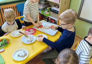 Dzieci siedzą przy stolikach i przygotowują kanapki