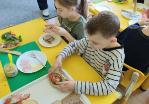 Dzieci siedzą przy stoliku i przygotowują kanapki