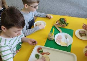 Chłopcy siedzą przy stoliku i przygotowują kanapki
