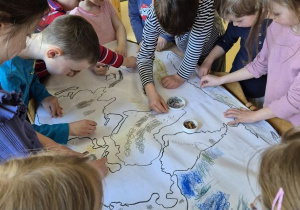 Dzieci stoją dookoła stołu i rysują wspólnie w grupie kilkuosobowej na dużym formacie