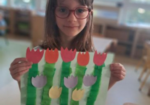 Dziewczynka prezentuje swoją pracę plastyczną przedstawiającą tulipany