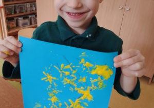 Chłopiec pozuje do zdjęcia trzymając swoją pracę plastyczną przedstawiającą forsycję