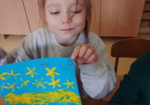 Dziewczynka pozuje do zdjęcia trzymając swoją pracę plastyczną przedstawiającą forsycję