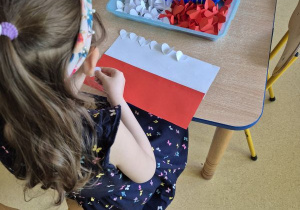 Dziewczynka przykleja białe serduszka do Flagi Polski