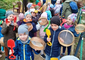 Dzieci trzymają w rękach sita i łopatki do poszukiwania kości dinozaurów w piasku