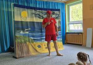 Dzieci siedzą na widowni i oglądają teatrzyk, na scenie ratownik wodny