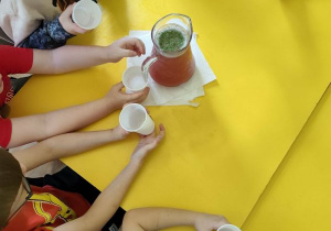 Dzieci siedzą przy stole i czekają na nalanie przygotowanego wcześniej napoju