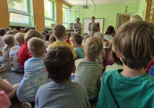 Dzieci siedzą na dywanie i słuchają informacji o bezpiecznym spędzaniu wakacji