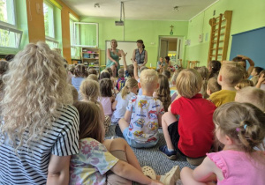 Dzieci siedzą na dywanie i słuchają informacji o bezpiecznym spędzaniu wakacji