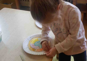 Dziewczynka koloruje papierowy talerzyk i wykonuje z niego ślimaka