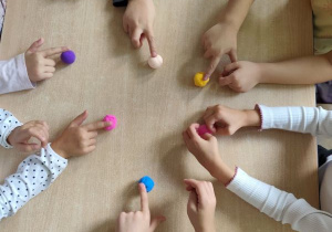 Dzieci wskazują palcem kolorowe kulki leżące na stole