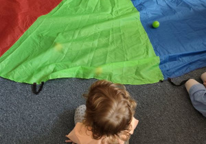 Dzieci siedzą dookoła chusty animacyjnej, na której leżą kolorowe piłeczki