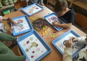 Dzieci siedzą przy stolę i rysują kropki według własnych pomysłów.