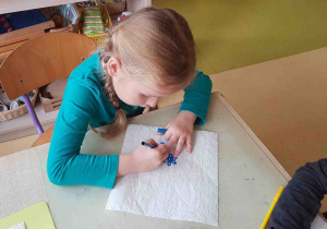 Dziewczynka wypełnia kawałek ręcznika papierowego kropkami, tworząc obrazek kwiatka